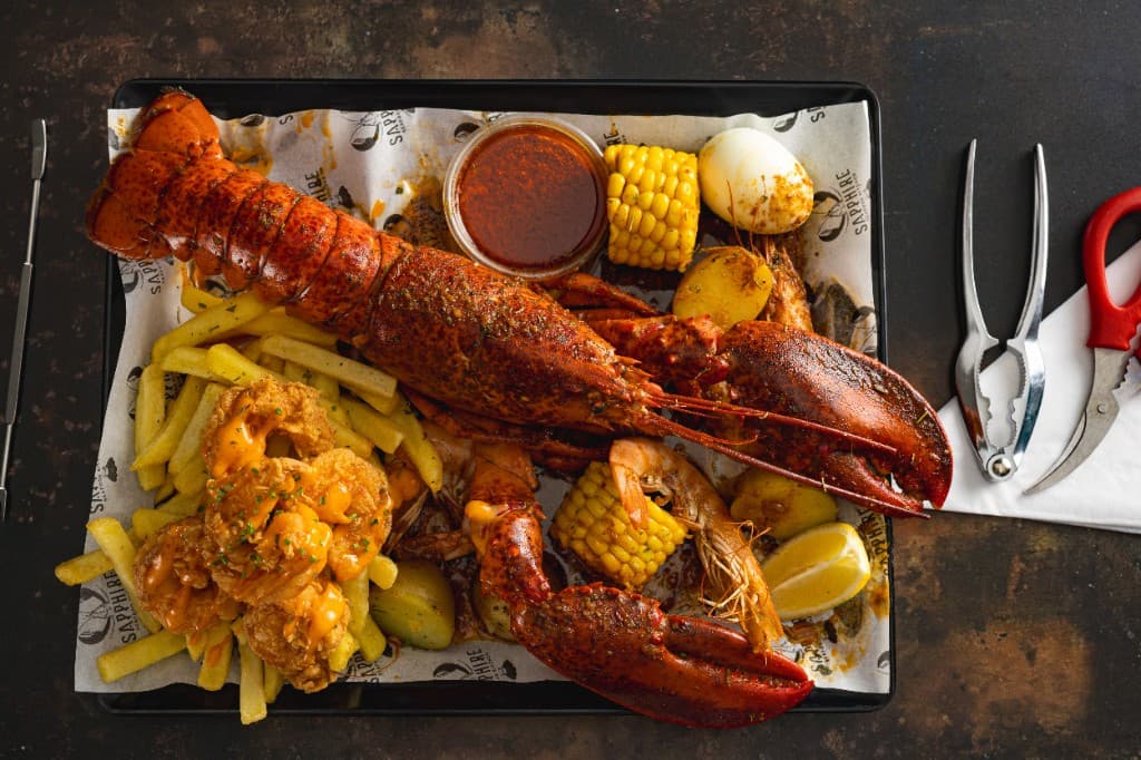 A whole seasoned lobster on Sapphire paper, with corn, fries, crackers, and red sauce